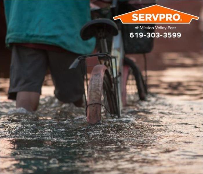 A person wades through the street with their bicycle.