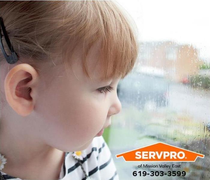 A child looks at the rain falling outside a window.