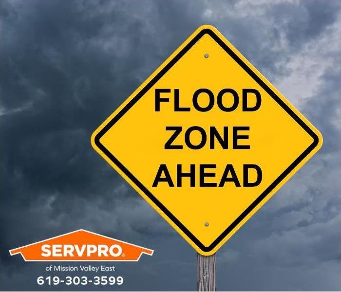 A yellow flood zone ahead sign stands on a stormy day.