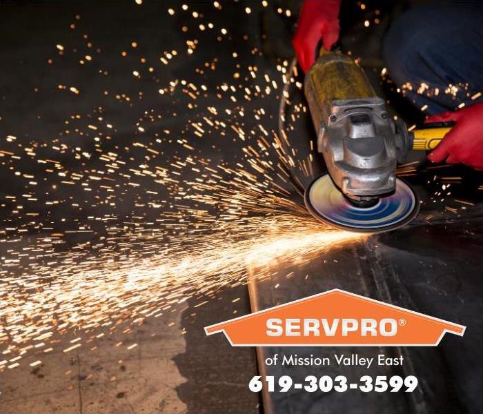 A worker is grinding a piece of metal that is throwing dangerous sparks of fire all around the shop.