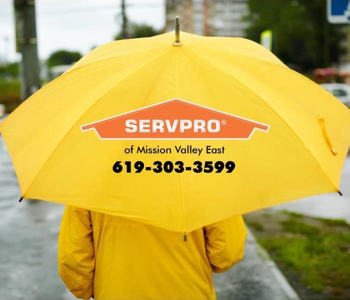 A person is shown walking down a wet and rain-drenched street with a yellow umbrella and wearing yellow rain gear. 