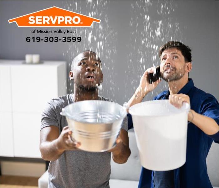 Two people hold buckets to catch water dripping from the ceiling.